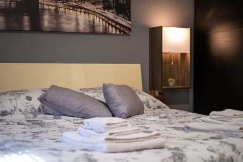 Modern bedroom at Navigli Affittacamere in Rozzano with cream headboard, patterned bedding, gray pillows, and warm wooden