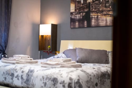Modern bedroom at Navigli Affittacamere in Rozzano with yellow headboard, gray pillows, white towels, wooden lamp, and city