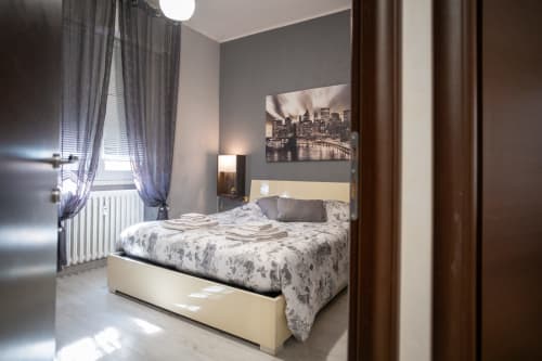 Modern bedroom at Navigli Affittacamere in Rozzano with cream bed, gray walls, city skyline artwork, and natural light