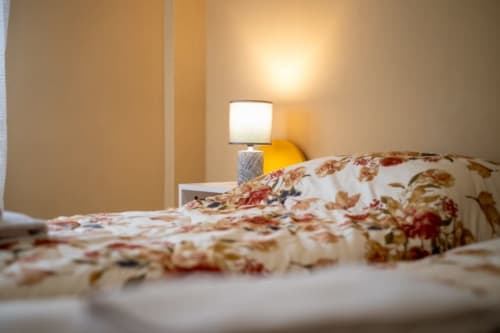 Accogliente camera da letto a Navigli Affittacamere a Rozzano con biancheria a fiori e lampada da comodino