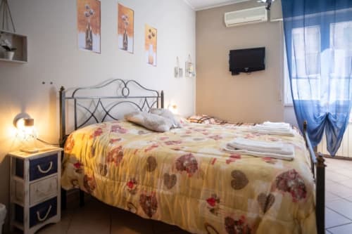 Bright bedroom at Navigli Affittacamere in Rozzano with metal bed frame, floral bedding, TV, and blue curtains