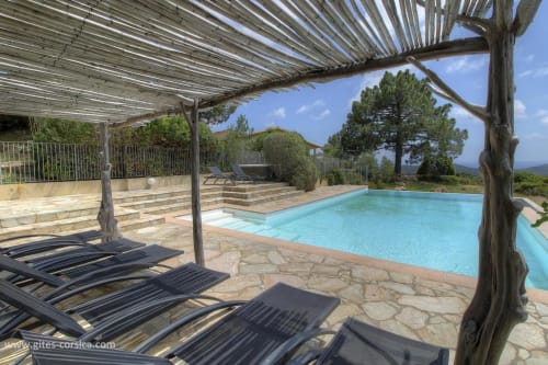Luxueux espace piscine à Vista D'oro à Monacia d'Aullène avec pergola, chaises longues et vue sur mer