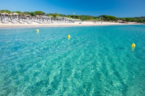 Eaux turquoise cristallines à la plage de Cavalaire-sur-Mer avec bouées jaunes et rivage sablonneux dominé par des falaises