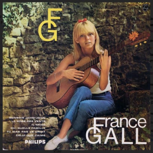 Young woman with blonde hair holding acoustic guitar against stone wall backdrop