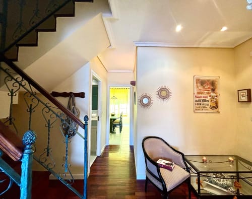 Elegante pasillo con barandilla de escalera de hierro forjado, paredes amarillas, espejos decorativos de rayos de sol y carteles vintage enmarcados