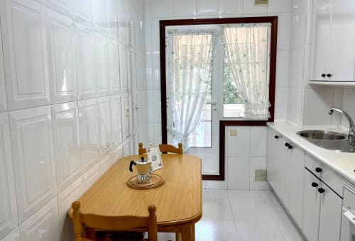 Comedor de cocina en apartamento Mariño, Baiona con mesa de madera, muebles blancos y acceso a terraza con vistas al mar