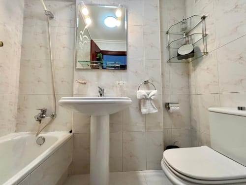 Baño moderno en apartamento Mariño, Baiona con lavamanos pedestal, espejo iluminado, inodoro, bañera y paredes alicatadas