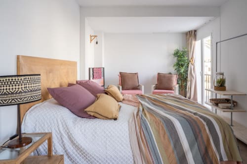 Espacioso dormitorio en Formentera Especial con cama de madera, manta rayada, almohadas moradas y zona de descanso con planta verde