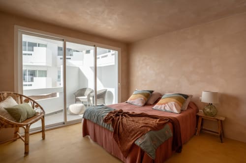 Dormitorio Luna en Formentera Especial con paredes de terracota, cama queen, silla de ratán y puertas de cristal al mar