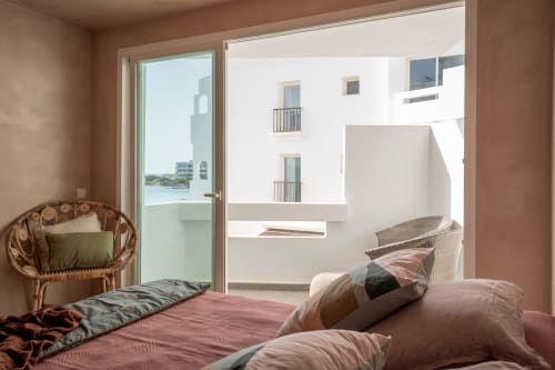 Habitación Luna Studio con balcón frente al mar de Formentera, silla de ratán, ropa de cama rosa y comodidades modernas
