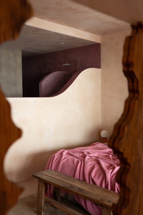 Dormitorio moderno en Formentera Especial con cabecera blanca curva, ropa de cama rosa, banco de madera y pared de acento oscuro