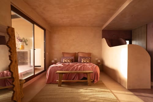 Dormitorio soleado en Formentera Especial con paredes de terracota, ropa de cama rosa, banco de madera y vista al mar desde el balcón en La