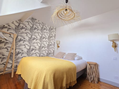 Bright bedroom with yellow bedcover, palm wallpaper, woven pendant light, and wooden floor at Relais des Îles cottage,