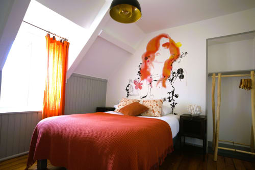 Modern bedroom at RELAIS DES ILES cottage with red bedding, artistic wall mural, and orange curtains in Saint-Marcouf
