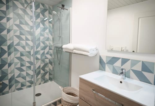 Modern bathroom at Relais des Îles cottage with geometric patterned tiles, glass shower, white sink vanity, and towel rack in