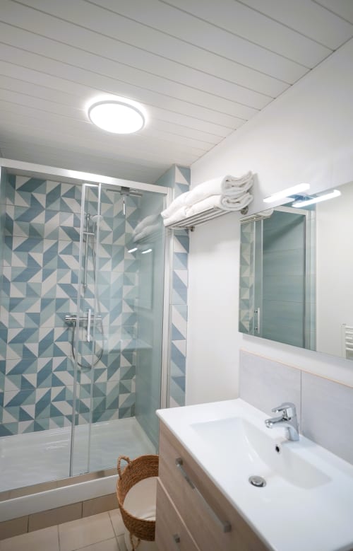 Modern bathroom at Relais des Îles cottage with geometric teal tile shower, white sink, and round ceiling light
