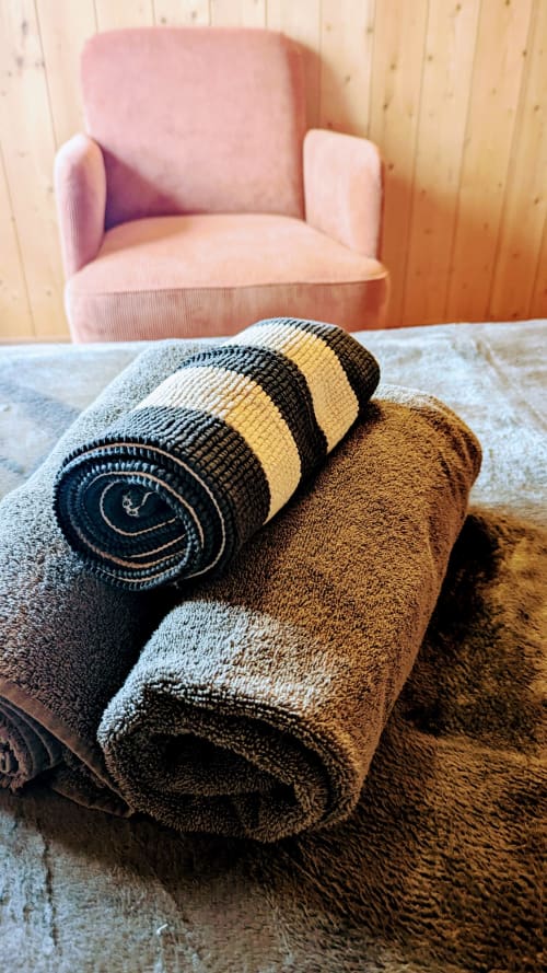 Rolled striped towels and brown linens displayed on table with pink armchair and wooden cabin interior at Belvédère