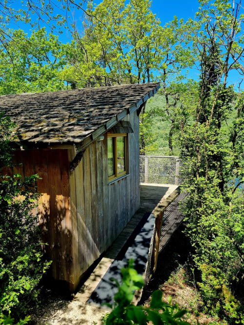 Wooden cabin nestled in forested hillside at Cabanes et lodges du Belvédère, Serrières-sur-Ain, with deck and mountain views.