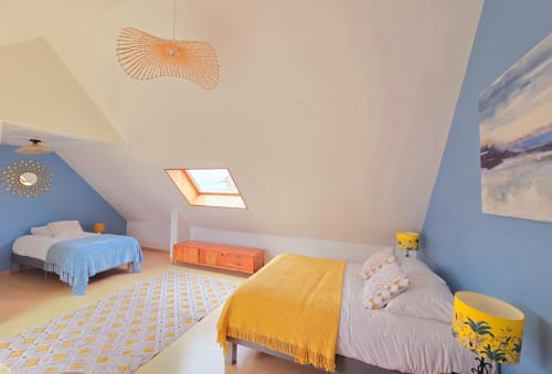 Bright attic bedroom at RELAIS DES ILES with two beds, yellow accents, skylights, and sea views from Saint-Marcouf cottage.