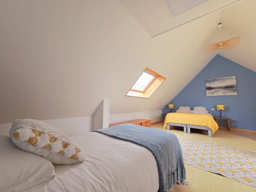 Bright attic bedroom at Relais des Iles cottage with sloped ceilings, skylights, two beds, and blue accent wall in