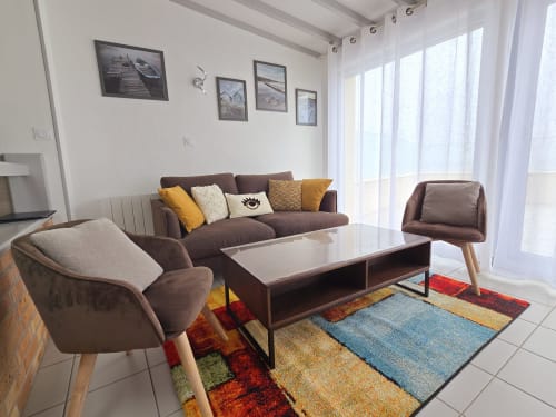 Modern living room at Relais des Îles cottage with brown sofa, armchairs, colorful rug, and sea views through large windows