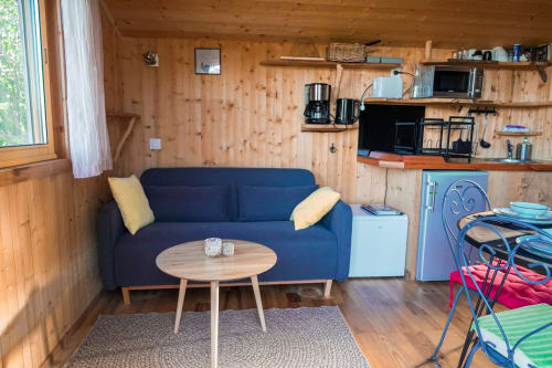 Cozy wooden cabin interior with blue sofa, coffee table, kitchenette, and shelving at Cabanes du Belvédère