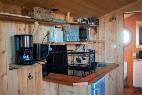 Rustic wood kitchenette with coffee maker, microwave, and storage shelves in La Pinede cabin, Serrières-sur-Ain