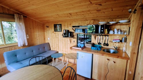 Wooden cabin interior with blue sofa, kitchenette, dining area, and mountain view at Cabanes du Belvédère, Serrières-sur-Ain