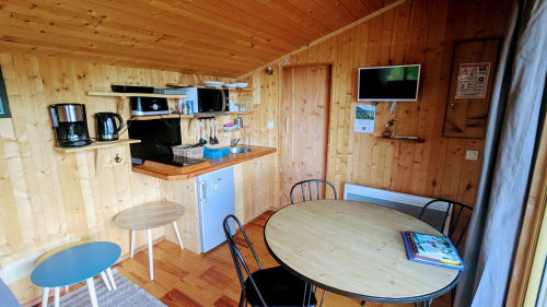 Cozy wooden cabin interior with dining area, kitchenette, and flat-screen TV at Cabanes du Belvédère, Serrières-sur-Ain