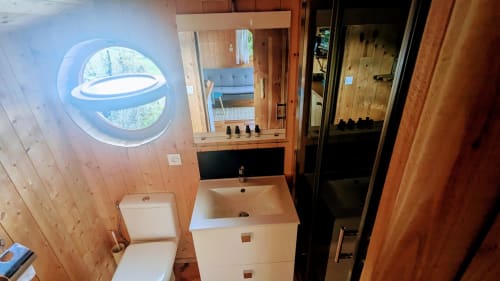 Modern bathroom with round porthole window, white sink, toilet, and wooden walls in LA SAPINIERE villa at Cabanes du