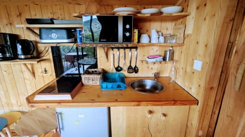 Wooden kitchenette in Cabane LA SAPINIERE with stove, sink, shelving, and cooking utensils at Belvédère lodge in