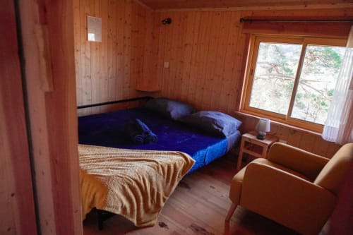 Cozy wooden cabin bedroom with blue bedding, wooden furnishings, and mountain views at Cabanes du Belvédère,