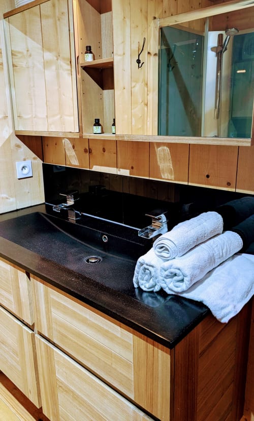 Modern bathroom vanity with black countertop, wooden cabinetry, dual mirrors, rolled white towels, and spa amenities at