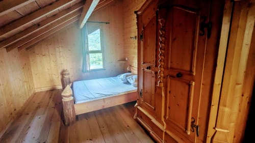Cozy wooden lodge bedroom with bed, rustic wood walls, window with mountain view, wardrobe, and wooden beams in