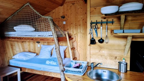 Interno rustico di una capanna in legno con letto a baldacchino, rete da pesca, biancheria blu, utensili da cucina e scaffalature