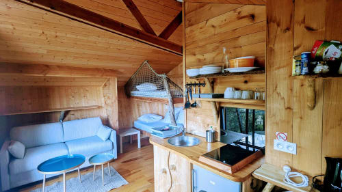 Interno accogliente di cabina in legno con angolo cottura, zona soggiorno e arredi blu a Cabanes du Belvédère