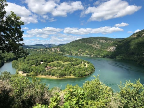 Curva del fiume turchese con colline boscose verdi e edifici sparsi a Serrières-sur-Ain, Francia