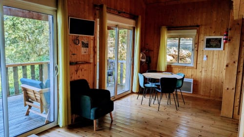 Interno di lodge in legno con tavolo da pranzo, poltrona e porte a vetri che si aprono sulla terrazza lacustre con vista su Serrières-sur-Ain