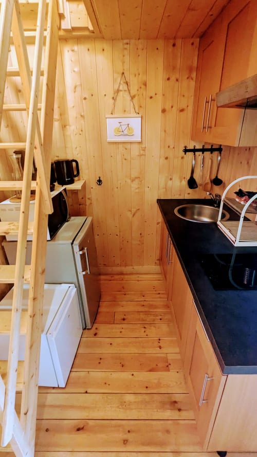 Compatta cucina di lodge in legno con piano cottura nero, lavello in acciaio inossidabile, utensili da cucina e arte della bicicletta alle Cabanes du