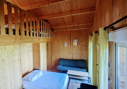 Camera rustica con letti blu, travi in legno e tende giallo-verde alle Cabanes du Belvédère