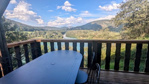 Terrazza in legno con vista sulla valle del fiume Ain, montagne, tavolo blu e bosco a Serrières-sur-Ain