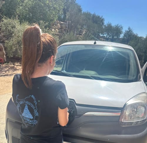 Woman at Su Barraccu agriturismo in Loceri, Italy, standing by white vehicle with rural surroundings
