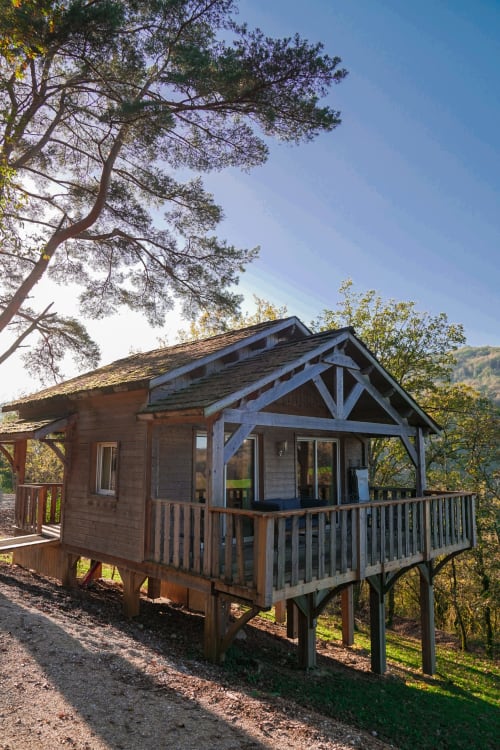 Cabane en bois surélevée avec véranda enveloppante sous les pins, Cabanes et lodges du Belvédère, Serrières-sur-Ain