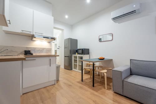 Modern studio apartment in Bordeaux with open kitchen, dining area, gray sofa, wooden floors, and air conditioning