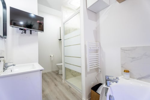 Modern bathroom at Wellkhome Bordeaux with sink, toilet, shower, towel rack, and wall-mounted TV