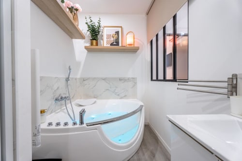 Modern bathroom at Wellkhome Appartements in Bordeaux featuring corner jacuzzi tub with blue lighting and marble accents