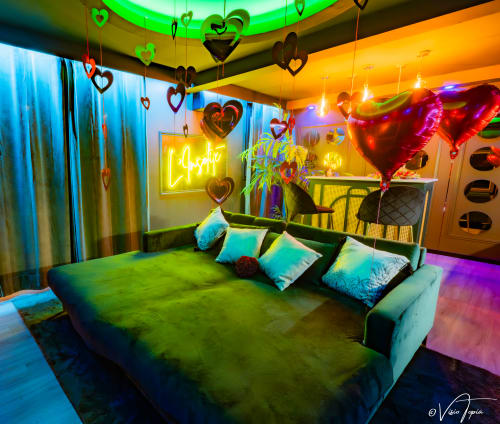 Chambre néon colorée au L'Insolite Spa Privatif de Toulouse avec lit vert, cœurs suspendus et éclairage vibrant rose-violet