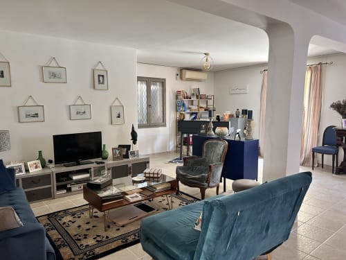Salon moderne de l'appartement d'Arles avec canapé bleu-vert, télévision, œuvres d'art, meuble de rangement bleu et vue sur le jardin