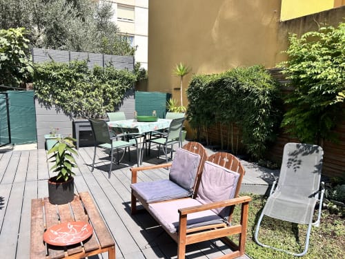Terrasse ensoleillée d'un appartement à Arles avec chaises longues en bois, table à manger, plantes et verdure