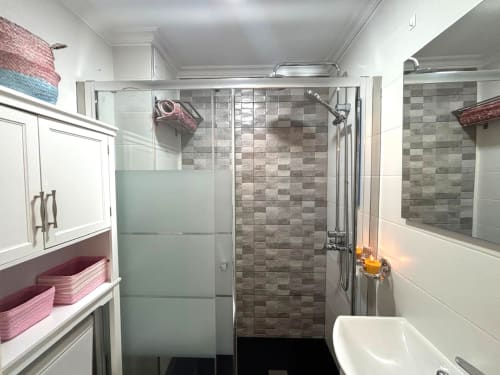 Baño moderno con ducha abierta, azulejos grises, tocador blanco y espejo en el apartamento Holibai Luceira de Baiona